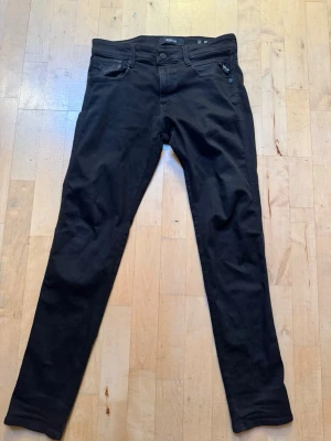 Replay anbass jeans  - Säljer ett par svarta slim fit jeans från Replay med klassisk femficksdesign och knappgylf. Jeansen har raka ben och diskret Replay-logga på bakfickan. Materialet är mjukt och stretchigt för extra komfort. Modellen är anbass och storleken är 30/32