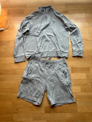 Grått loungewear-set från Polo Ralph Lauren - Mysigt grått loungewear-set från Polo Ralph Lauren med långärmad tröja med halv dragkedja och matchande shorts med dragsko i midjan. Båda delarna har diskret logga broderad framtill och är tillverkade i mjukt bomullsmaterial. Perfekt för chill dagar hemma. Säljer då det inte passar längre. Inga fläckar. Säljer båda för 500kr ny pris halfzip1700kr och nypris shorts 1200kr. Allting äkta 