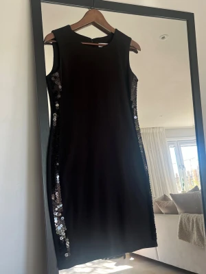Calvin Klein ärmlös klänning  - Snygg svart ärmlös klänning med paljettdetaljer längs sidorna. Klänningen har en rak, klassisk passform och är tillverkad i ett mjukt material som ger en elegant look. Stor i modellen 