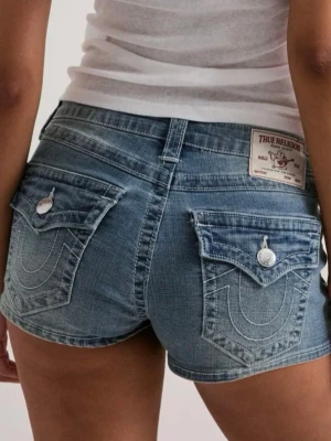 Blå jeansshorts från True Religion - Säljer ett par blå jeansshorts från True Religion med klassiska kontrastsömmar och stora fickor med lock och knapp bak. Shortsen har en casual denimlook och ett patch med logga bak i midjan. Perfekta för sommaren! Storlek 25