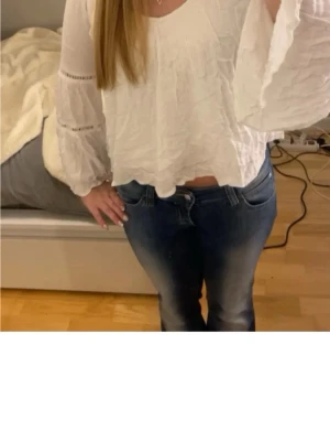 Hollister blus - Säljer en vit blus med v-ringning och vida, långärmade ärmar. Blusen har ett krinklat tyg och dekorativa spetsdetaljer på ärmarna. Perfekt till jeans för en avslappnad men trendig look.