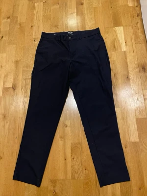 Svarta  kostymbyxor Jack&Jones stl W34 L32  - Snygga svarta  kostymbyxor från Jack&Jones med klassisk rak passform. Byxorna har två sidofickor fram och två bakfickor med knapp. Perfekta för en stilren look. Materialet är mjukt och har en lätt stretch för extra komfort.
