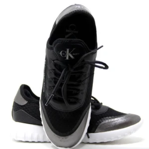 Svarta Calvin Klein sneakers - Snygga svarta sneakers från Calvin Klein med vita sulor och grå detaljer. Ovandelen är i mesh och syntetmaterial för en sportig look. Klassisk snörning och låg modell med diskret CK-logga på plösen.