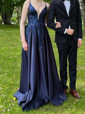 Mörkblå långklänning med paljetter - Säljer nu min fantastiska balklänning. Elegant långklänning i mörkblått med smala axelband och djup v-ringning. Endast använd en gång men har tillkommit en små defekter. Paljetter som släppt från klänningen vid ena axelbandet samt ett litet hål (nästan obefintligt) vid bysten. Storlek US4 och specialsydd för mig som är 182 cm lång