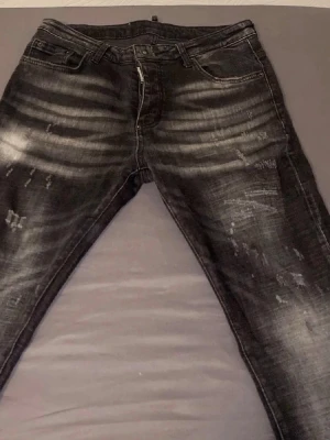 Svarta slitna jeans med tvättade detaljer - Säljer ett par svarta jeans med coola slitningar och tvättade detaljer. Jeansen har klassisk femficksmodell och dragkedjegylf. Perfekta för dig som gillar en lite tuffare streetstil.