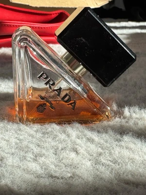 Prada Paradoxe Intense Parfym - Prada Paradoxe intense från Prada i en genomskinlig triangelformad glasflaska med svart, fyrkantigt lock. Flaskan har en elegant orangefärgad vätska och tydlig Prada-logga på framsidan. Perfekt för dig som gillar exklusiva och stilrena dofter.