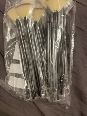Set med svarta solfjäderformade sminkborstar - (10kr STYCK) Ett set med flera solfjäderformade sminkborstar med svarta handtag och ljusgula borst med mörkare toppar. Borstarna är förpackade i plast och har syntetiska strån som passar perfekt för highlighter eller contouring. Snygg och stilren design som gör sminkrutinen enkel.