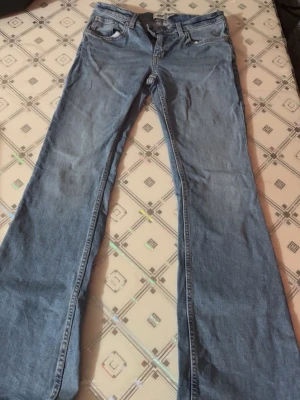 Ljusblå bootcut jeans - Säljer ett par ljusblå bootcut jeans med klassisk femficksdesign och normalhög midja. Jeansen har utsvängda ben och är tillverkade i denim. Perfekta för dig som gillar en retroinspirerad stil.