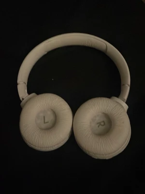 Vita over-ear hörlurar från JBL - Säljer ett par vita over-ear hörlurar från JBL. De har en mjuk vadderad båge och stora öronkuddar med tydlig L och R-markering. Hörlurarna är tillverkade i plast och konstläder, och har en stilren, rundad design.