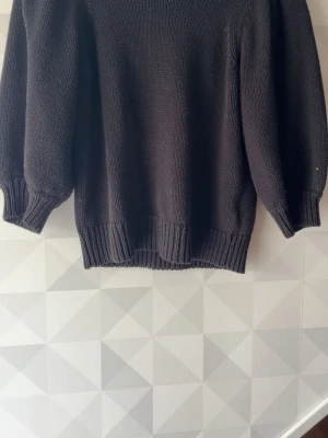 Svart stickad tröja från Gina Tricot - Mysig svart stickad tröja från Gina Tricot med rund halsringning och breda ribbade muddar vid ärmslut och nederkant. Perfekt för lager-på-lager och enkel att matcha med jeans eller kjol.
