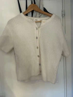Vit kofta i ullmix från Gina Tricot - Superfin vit kofta från Gina Tricot i mjuk ullblandning. Kortärmad modell med rund hals och knappar framtill. Perfekt att styla över ett linne eller t-shirt för en chill look.