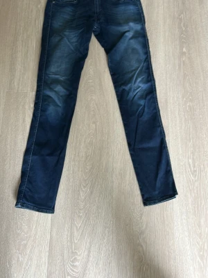 Replay anbass - Snygga mörkblå jeans med raka ben och klassisk femficksdesign. Jeansen har en lätt tvättad look med diskreta slitningar framtill och bakfickor. Perfekta för en avslappnad och trendig stil. Storlek 32/34