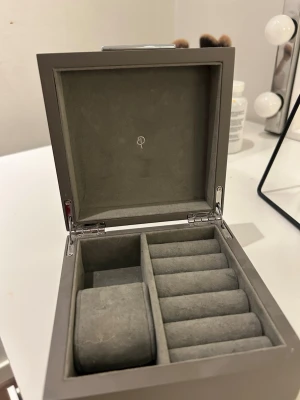 Grå klocklåda i sammet från Edblad  - Snygg och stilren klocklåda i grå sammet med plats för flera klockor. Lådan har mjuka fack och en kudde för att skydda och organisera dina accessoarer. Perfekt för att hålla koll på dina favoriter och ge en lyxig känsla till din förvaring.