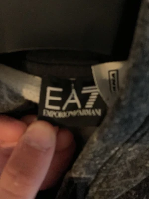Svart hoodie från EA7 Emporio Armani - Snygg svart hoodie från EA7 Emporio Armani med unikt mönster och huva. Hoodien har en cool tvättad look och är tillverkad i mjukt material som känns skönt mot huden. Perfekt för dig som vill ha en stilren och trendig look.