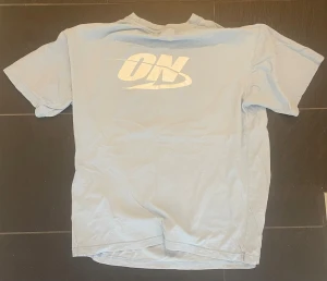 Ljusblå t-shirt med ON-tryck - Ljusblå t-shirt med stort vitt ON-tryck på ryggen. Klassisk passform med korta ärmar och rund hals. Perfekt för en avslappnad och sportig stil.