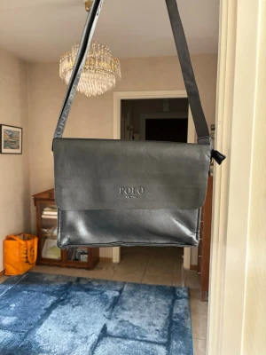 Svart dator väska från Polo - Snygg svart dator väska från Polo med stilren design. Väskan är tillverkad i slätt konstläder och har ett lock med Polo-logga framtill. Justerbar axelrem och dragkedja baktill för extra förvaring. Perfekt för dig som vill ha en klassisk och enkel look.