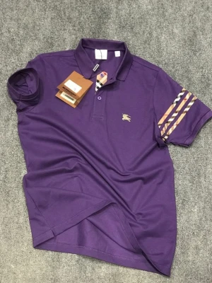 Lila pikétröja från Burberry - Säljer en lila pikétröja från Burberry med klassisk krage och knappslå. Tröjan har korta ärmar med Burberrys rutiga detaljer på ena ärmen och insidan av kragen. Ikonisk logga broderad på bröstet.