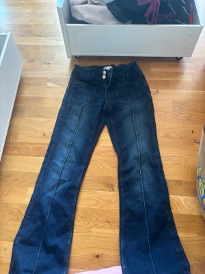 Mörkblå bootcut jeans Gina Tricot - Snygga mörkblå bootcut jeans från Gina Tricot med hög midja och dekorativa sömmar framtill. Jeansen har stora framfickor och dubbla knappar i midjan. Perfekta för en trendig och avslappnad look.