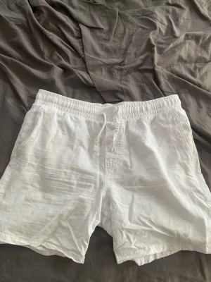 Vita linne-shorts med snörning - Säljer ett par vita shorts i linne med snörning i midjan. De har en relaxed passform och sidofickor, perfekta för varma dagar. Materialet är lätt och luftigt, vilket gör dem riktigt sköna att bära.