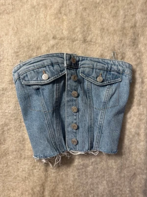 Ljusblå topp med rå kant - Säljer en  ljusblå topp med rak passform och trendig rå kant nertill. Jeansen har klassisk femficksdesign och är tillverkade i denim. Perfekta för en avslappnad och cool stil.