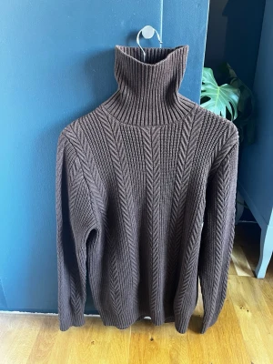 Brun stickad polotröja från HM - Mysig brun stickad polotröja från HM med höga ribbade detaljer. Tröjan har långa ärmar och hög polokrage som ger extra värme. Perfekt för kalla dagar och sommar kvällar. 