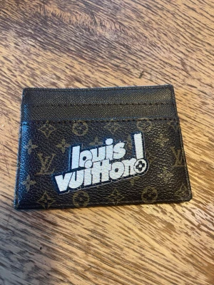 Unik sälsynt monogram korthållare - Snygg korthållare  i klassiskt brunt monogrammönster med vit grafisk logga på framsidan. Tillverkad i tåligt canvasmaterial och har flera kortfack. Perfekt accessoar för dig som gillar lyxiga detaljer. Superfin. Använd köp nu