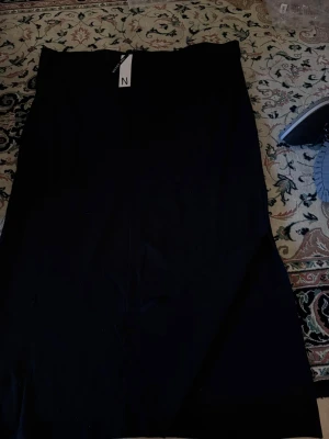 Svart långkjol från Nelly - En stilren svart långkjol från Nelly. Kjolen har en klassisk rak passform och är perfekt för dig som gillar en enkel och tidlös look. Materialet känns mjukt och följsamt, vilket gör den bekväm att bära hela dagen.