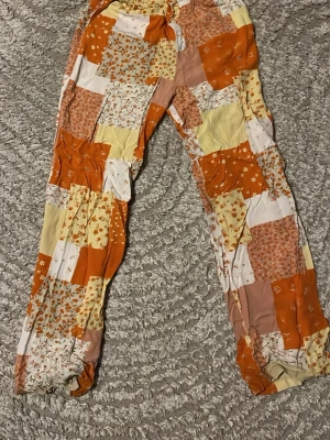 Patchwork mjukisbyxor från Monki - Färgglada mjukisbyxor från Monki i patchwork-stil med orange, gul, vit och rosa mönster. Byxorna har resår i midjan och vid benslut, samt blommiga och rutiga detaljer. Perfekta för en chill och avslappnad look.