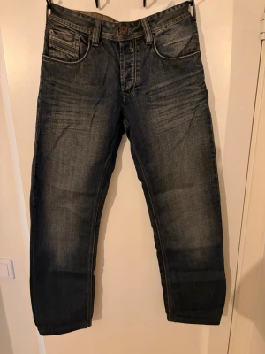 Blå jeans från FSBN med raka ben - Säljer ett par blå jeans från FSBN med snygg tvätt och raka ben. Jeansen har klassiska fem fickor, kontrastsömmar och coola detaljer på bakfickorna. Materialet är slitstark denim i bomull. Perfekta för en avslappnad och trendig look.