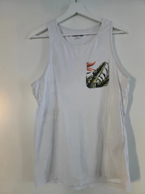 Vit linnetopp från Jack & Jones - Säljer en vit linnetopp från Jack & Jones i bomull. Toppen har en cool bröstficka med tropiskt mönster i grönt och orange. Perfekt för sommarens alla äventyr och enkel att matcha med jeans eller shorts.