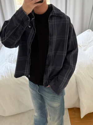 Mörkblå rutig overshirt från Zara - Snygg mörkblå overshirt från Zara med diskret rutmönster i grått. Overshirten har klassisk krage, dragkedja framtill och avslappnad passform. Perfekt att bära över en t-shirt för en chill och trendig look.