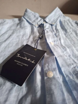 Ljusblå linneskjorta från Bondelid - Säljer en ljusblå skjorta från Bondelid i svalt linne. Skjortan har klassisk krage, vita knappar och en avslappnad passform. Perfekt för dig som gillar stilrena och bekväma plagg. Taggen sitter kvar.