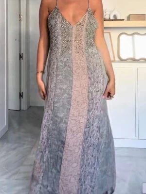 Långklänning - Säljer en elegant långklänning med smala axelband och djup v-ringning. Klänningen har glittriga detaljer upptill. Perfekt för dig som vill sticka ut med en unik och lyxig look. Oanvänd med prislapp kvar