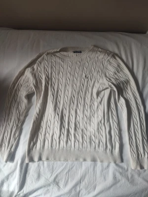Stickad tröja från GANT - Tröjan är cremévit. Stickad vit tröja från GANT med rund halsringning och broderad logga på bröstet. Premium cotton. Har knappt använt den då den är för stor.