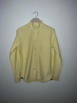 Morris skjorta  - Snygg ljusgul skjorta från Morris med klassisk krage och knäppning framtill. Skjortan har långa ärmar och en liten broderad Morris logga på bröstet .skjortan är gjord i 100% bomull Perfekt för dig som vill ha en stilren och fräsch look inför sommaren!