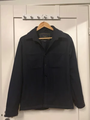 Mörkblå overshirt från donce de la sense - Stilren mörkblå overshirt från donce de la sense nypris: 1500kr med klassisk krage, knäppning framtill och två bröstfickor. Overshirten har en rak passform och är tillverkad i ett mjukt tyg som ger en avslappnad men snygg look. Saknas en knapp längs ner men annars helt ny.🔥🤩👔