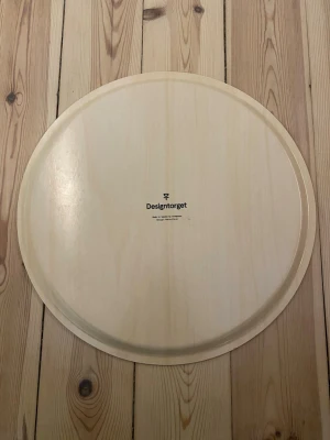 Runda brickor från Designtorget - Snygg rund serveringsbricka från Designtorget. Ena sidan är ljus träfärgad med tryckt logga, andra sidan är svart med små vita prickar. Perfekt för att servera fika eller frukost på sängen. 