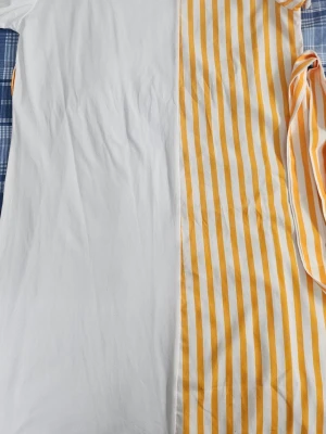 Vit och gulrandig t-shirt - T-shirt med unik design där ena sidan är helvit och andra sidan har gula och vita ränder. Modellen är rak och har klassisk t-shirtform. Tillverkad i mjukt bomullstyg som känns skönt mot huden. Perfekt för dig som gillar färg och kontraster.
