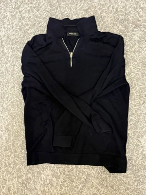 Svart halvzip-tröja Massimo Dutti - Stilren svart tröja från Massimo Dutti med halv dragkedja och hög krage. Tröjan har långa ärmar och ribbade muddar. Perfekt för en clean och klassisk look. Materialet känns mjukt och bekvämt.