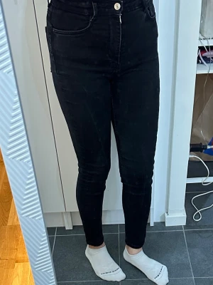 Svarta skinny jeans från Gina Tricot - Säljer ett par svarta skinny jeans från Gina Tricot med hög midja och klassisk femficksdesign. Jeansen har dragkedja och knapp framtill samt smal passform hela vägen ner. Perfekta till en trendig och avslappnad stil.
