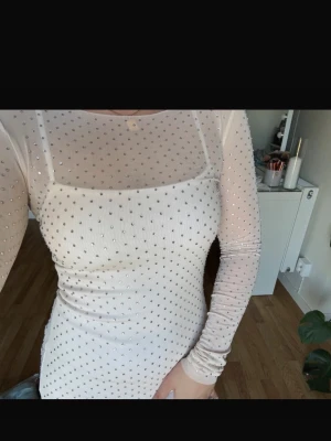 Vit glittrig meshklänning - Klänning med glittriga detaljer och mesh-tyg. Klänningen har långärmade meshpartier och en tight passform som framhäver figuren. Perfekt för dig som vill sticka ut med en elegant och modern look.