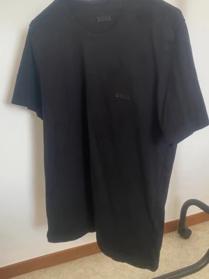 Svart t-shirt från BOSS - Säljer en svart t-shirt från BOSS med diskret logga på bröstet. T-shirten har klassisk rund hals och korta ärmar, perfekt för en clean och stilren look. Materialet är mjukt och känns skönt mot huden.