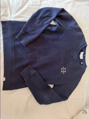 Mörkblå sweatshirt från Les Deux Storlek S - Mörkblå sweatshirt från Les Deux med broderad logga i vitt på bröstet. Klassisk rund halsringning och ribbade muddar vid ärmslut och nederkant. Perfekt för en avslappnad och stilren look. Storlek small, pris kan diskuteras