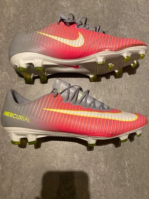 Nike Mercurial fotbollsskor röd/grå - Säljer ett par Nike Mercurial fotbollsskor i rött och grått med gula detaljer och vita sulor. Skorna är som nya! 