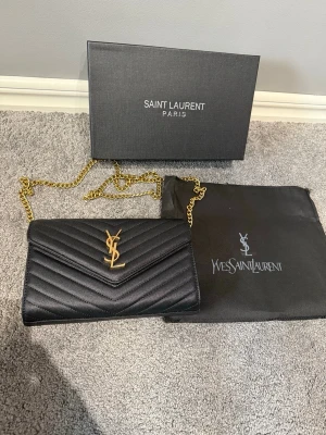 Svart kuvertväska från Saint Laurent - Skit snygg svart kuvertväska från Saint Laurent med guldfärgad kedja. 