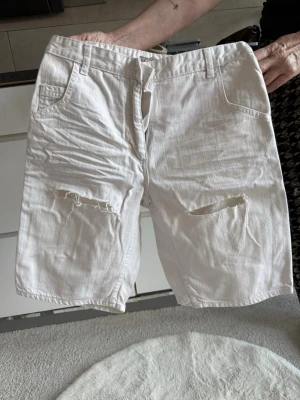 Vita shorts med slits från H&M (S) - Säljer ett par vita shorts från H&M i storlek 36. De har slitsar och slitna detaljer på framsidan, klassisk femficksdesign och snörning i midjan. 