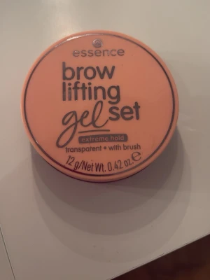 Essence Brow Lifting Gel Set Transparent - Essence brow lifting gel set med extrem stadga. Transparent gel som formar och fixerar brynen, levereras i en rund burk med tillhörande borste. Perfekt för att skapa lyfta och definierade ögonbryn. Innehåller 12 g. Det är mer än hälften kvar av gelet men man ser på borsten att den är använd. Går säkert att tvätta med tvål för att få bort.