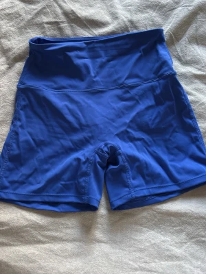 Blå träningstights shorts från Relode - Säljer ett par blå tränings shorts från Redlode med hög midja och scrunch-detalj bak. Tillverkade i stretchigt funktionsmaterial som passar perfekt för gym eller löpning.