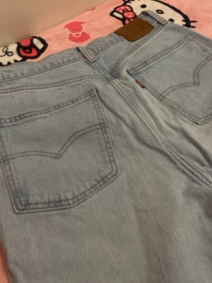 Levi's ljusblå raka jeans - Säljer ett par klassiska ljusblå jeans från Levi's med raka ben och hög midja. Jeansen har två bakfickor med den ikoniska sömmen och en brun läderpatch med Levi's-loggan bak i midjan. Perfekta för en avslappnad och trendig look.