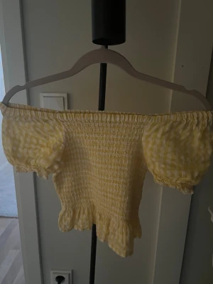 Gul offshoulder topp med volang - En jätte söt gul kort  topp perfekt till sommaren, man kan ha den både offshoulder men också över axlarna, den e gul rutig o har lite volang längst nere, storleken är borta men passar mig som är 152( skulle gissa på att storleken är runt 146-152( skriver in Xxs i storlek men den passar mig som bär från 152/xxs,xs,s